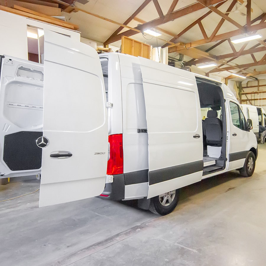 White Mercedes Sprinter van with the back and side doors open while parked inside our shop.